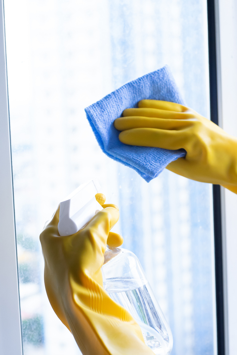 Hands in Gloves Holding Spraying Bottle and Towel Cleaning Window